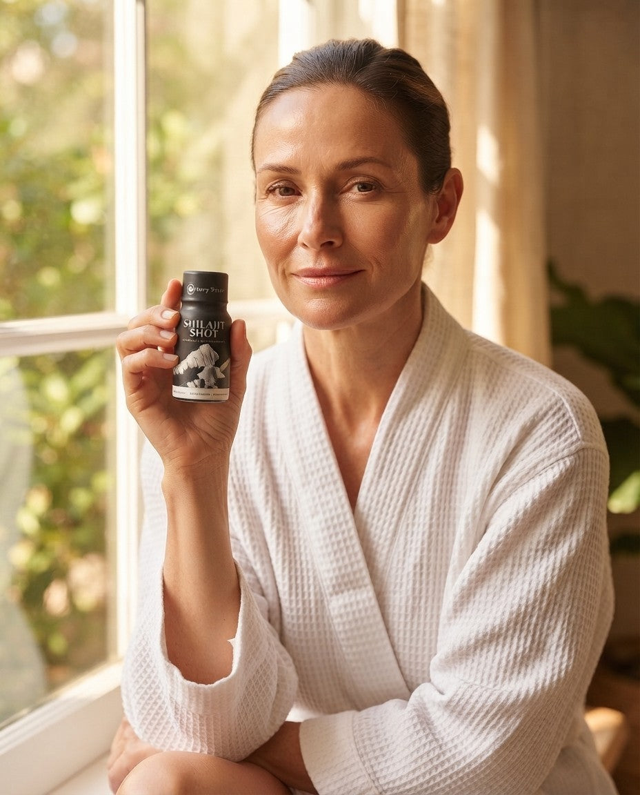 Woman in a white robe by a sunny window holding a Holy Shilajit Shilajit Shot