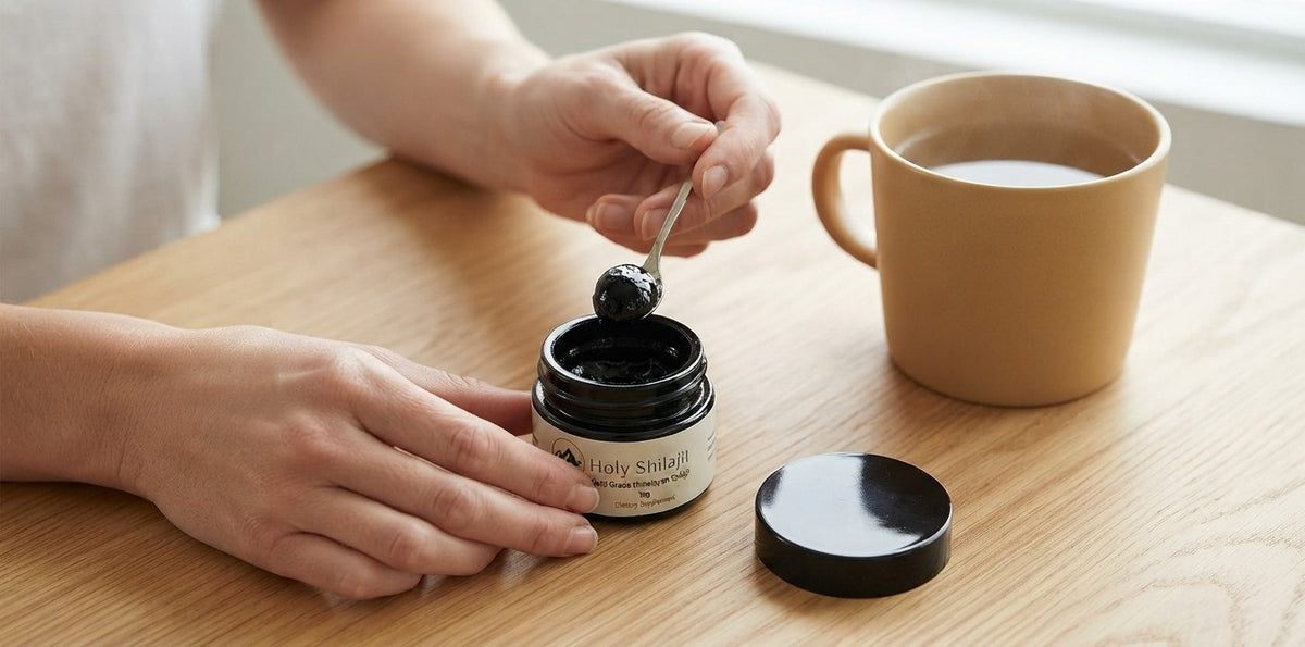 Scooping a pea-sized piece of shilajit resin from the jar beside a mug of hot water